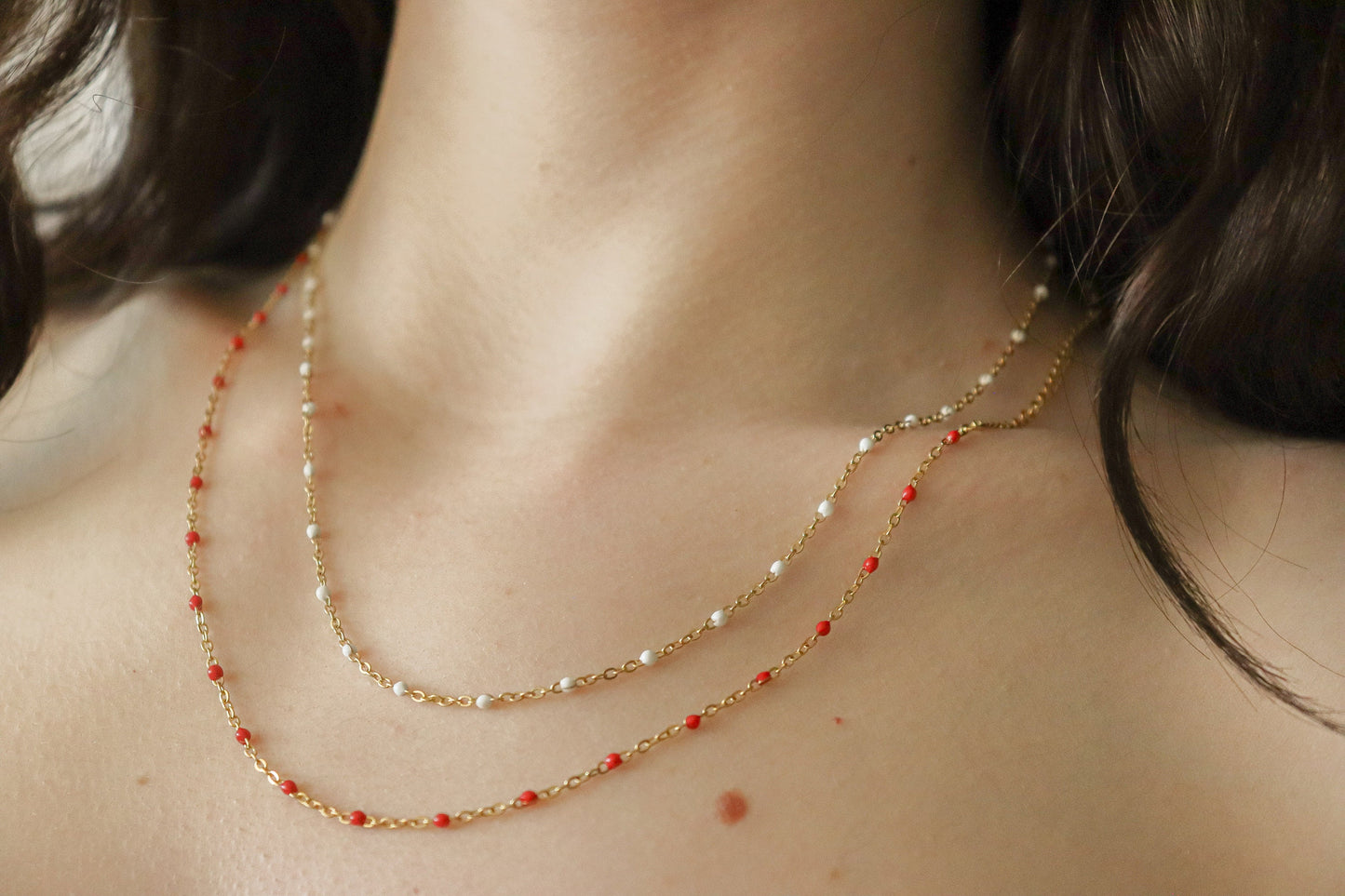 May include: Two gold chains with red and white beads.